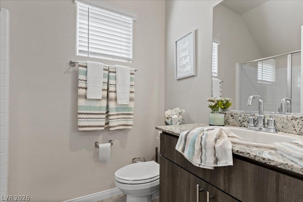 A well-appointed bathroom featuring a single vanity with granite counters and a practical commode.