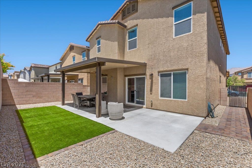 An inviting outdoor living space features a covered patio, artificial turf, and low-maintenance landscaping.