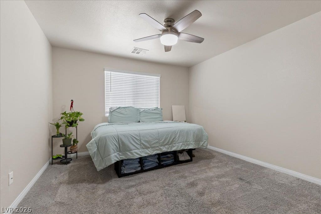 A well-lit bedroom with comfortable carpeting features a ceiling fan and ample window light.