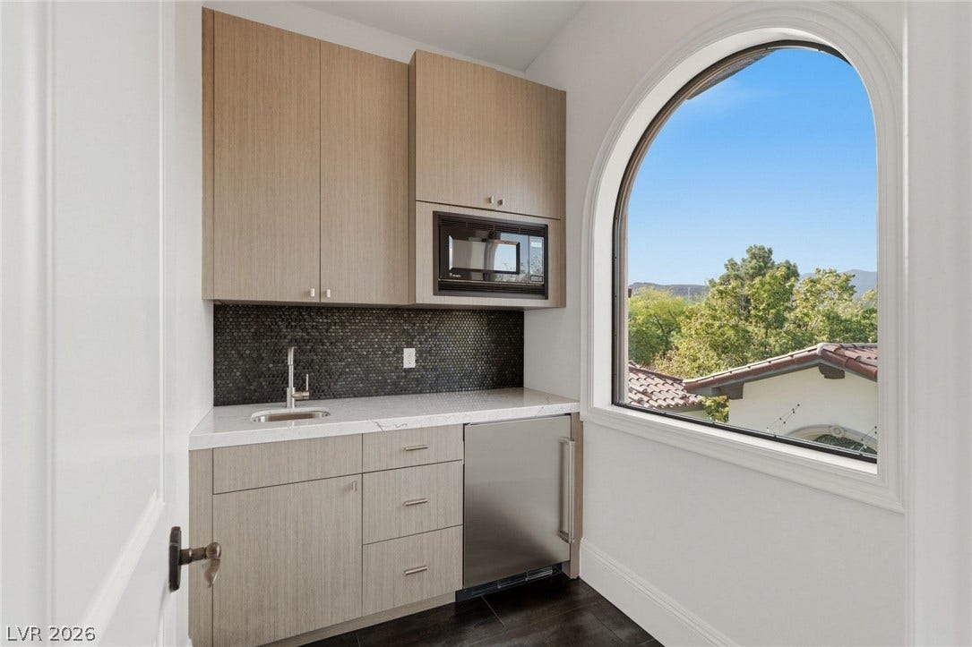An arched window frames serene hillside views beside a modern wet bar setup.