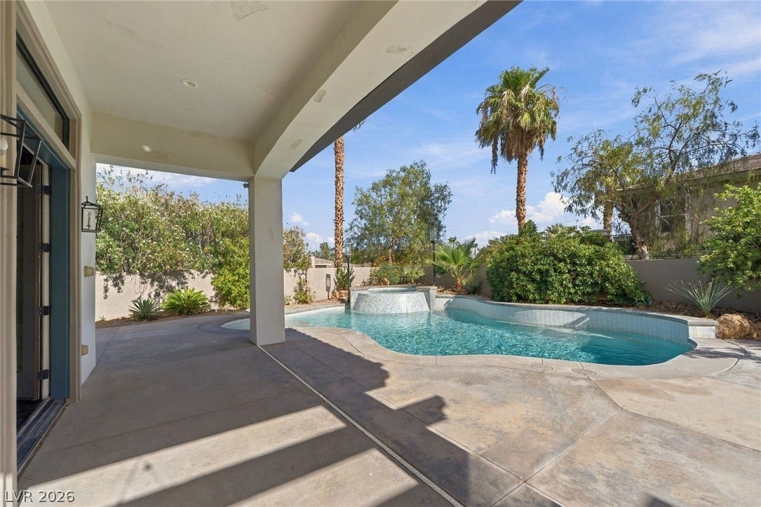 A covered patio overlooks a custom swimming pool with integrated spa and mature landscaping.
