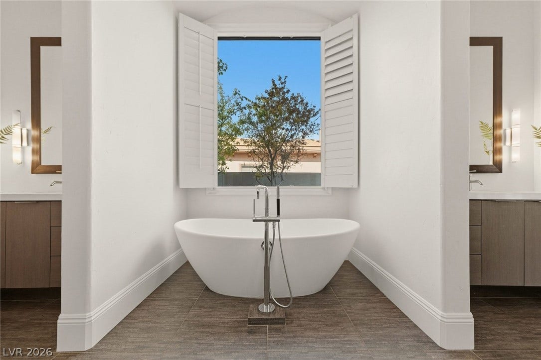 An elegant freestanding soaking tub centers the space under a window with plantation shutters.