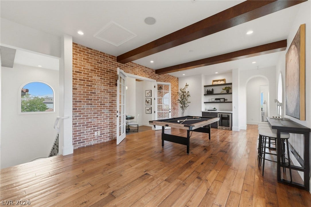 Rich hardwood floors complement an exposed brick accent wall and exposed wooden ceiling beams.
