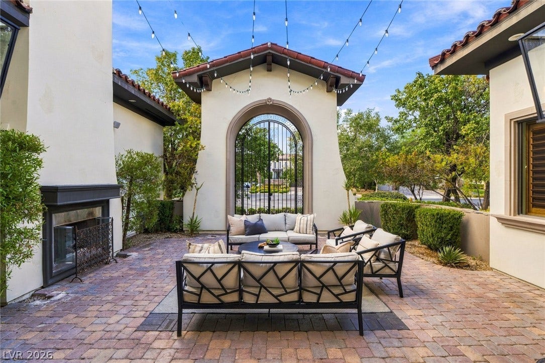 An inviting stone-paved courtyard is anchored by a stately outdoor fireplace and arched iron gate.