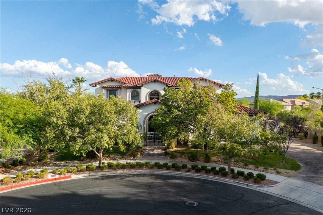 Stately Spanish tile roof architecture framed by mature trees along a paved neighborhood cul-de-sac.