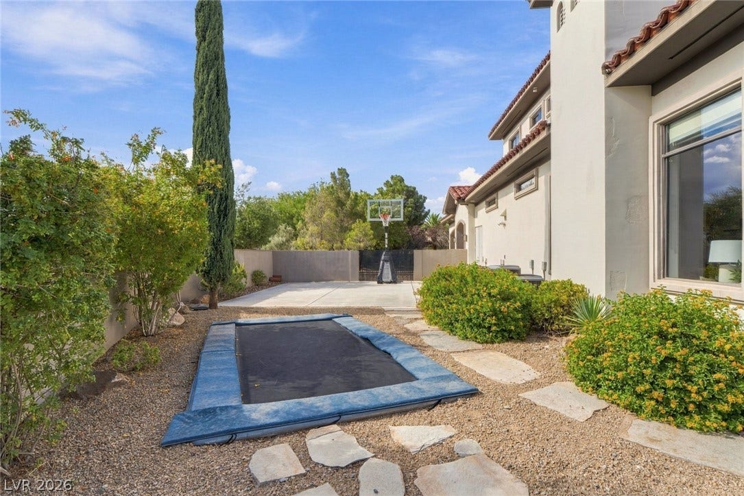 A spacious side yard incorporates stone pathways, native landscaping, and a concrete sport court.