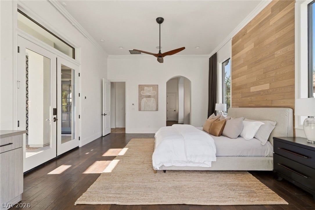 Rich hardwood floors and a wood-paneled accent wall define this airy principal bedroom.