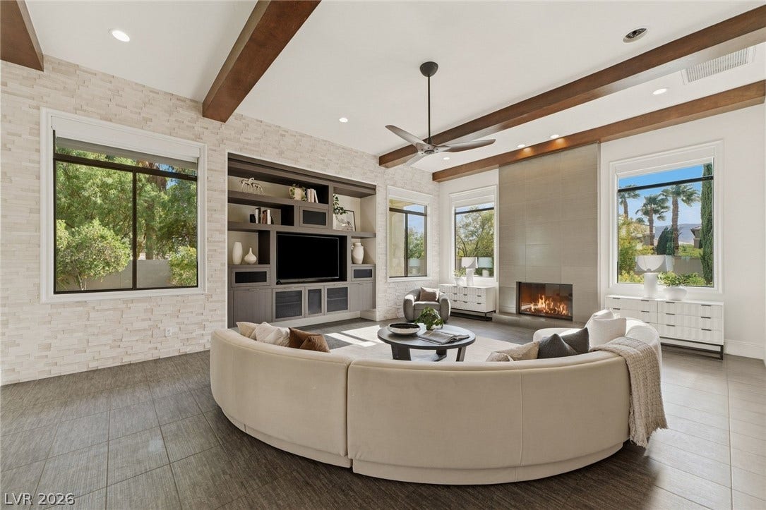 Rich wood ceiling beams and a sleek modern fireplace define this open living space.
