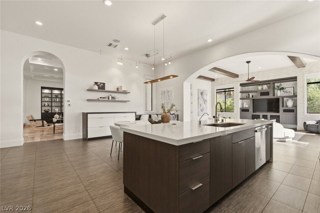 An expansive kitchen features a large central island and smooth tile flooring under recessed lighting.
