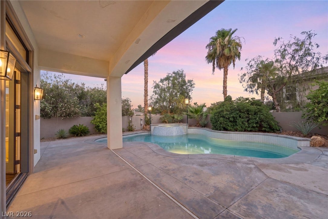 An inviting covered patio steps down to a custom swimming pool with a raised spa.