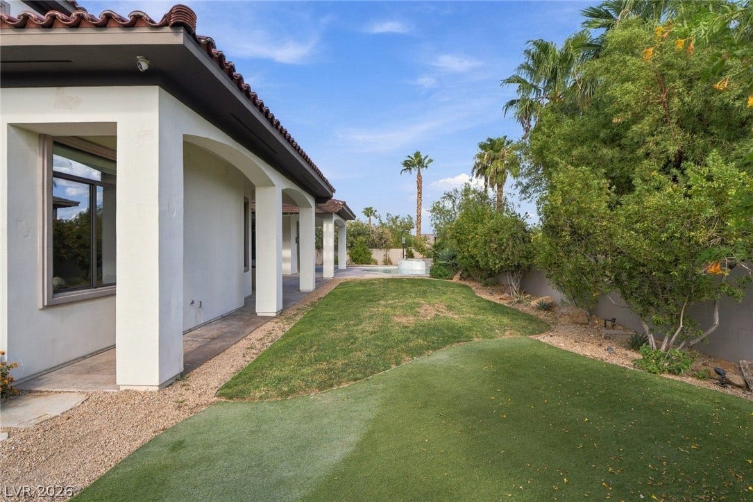 Manicured green lawn borders a covered patio beneath Spanish tile roofing details.