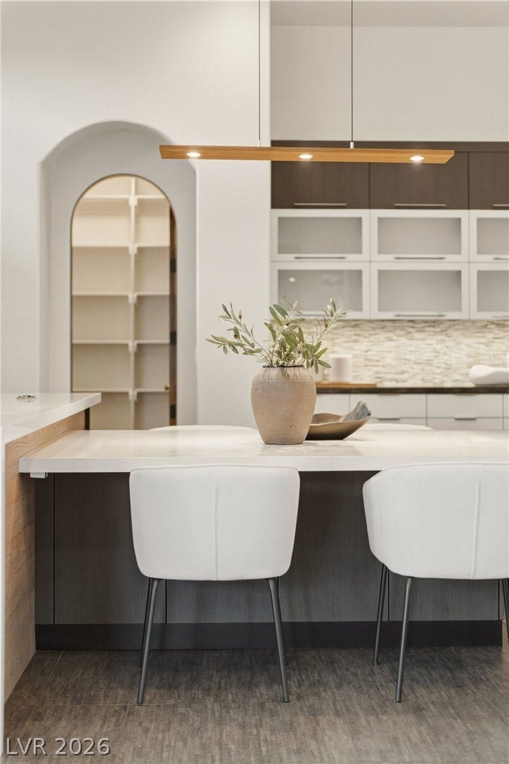An arched doorway leads to a walk-in pantry adjacent to the modern kitchen island.