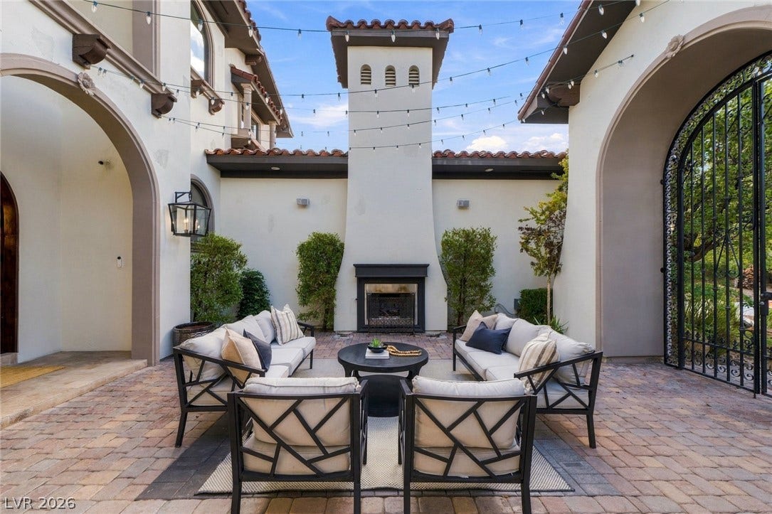 An inviting courtyard features brick paving and a grand outdoor fireplace under the open sky.