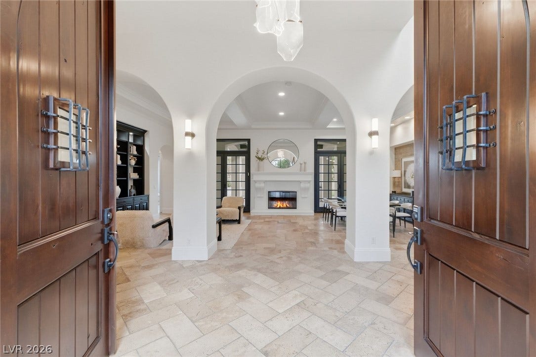 Double doors open to an entry showcasing arched passages, tile floors, and a distant fireplace.