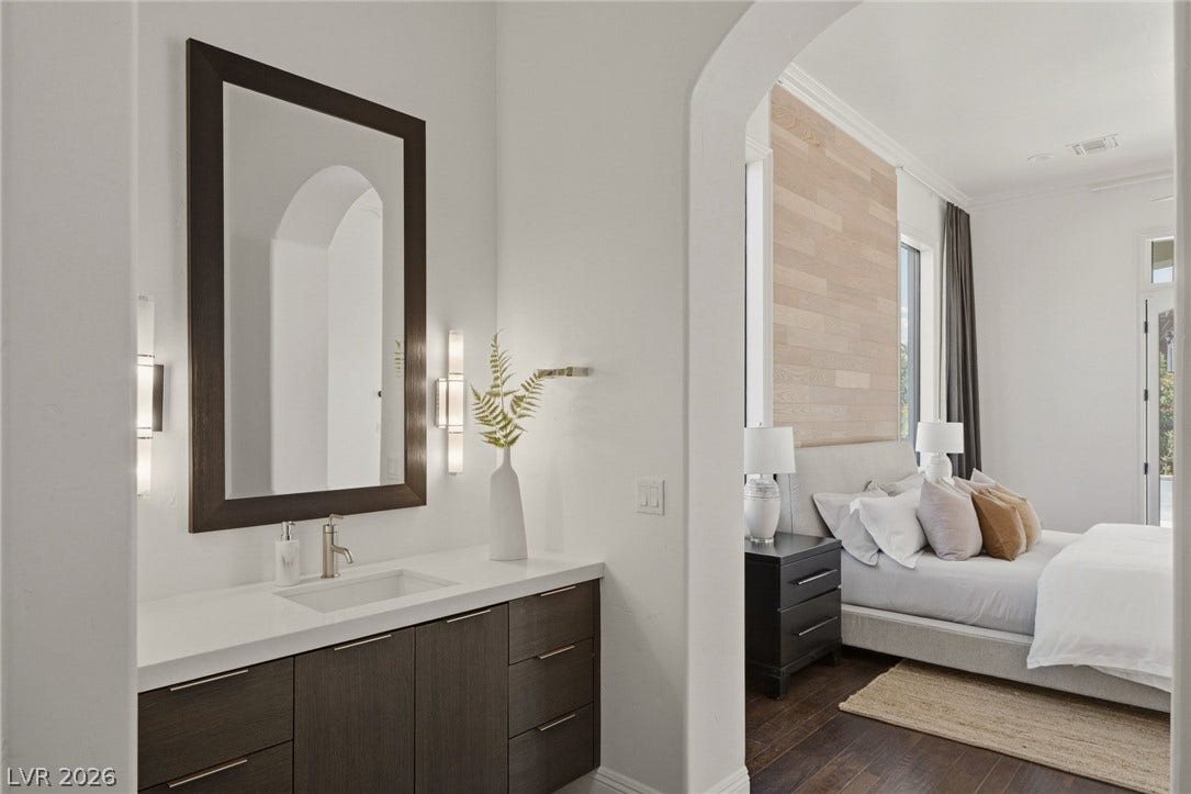 An arched doorway connects a clean vanity station to the hardwood-floored suite beyond.