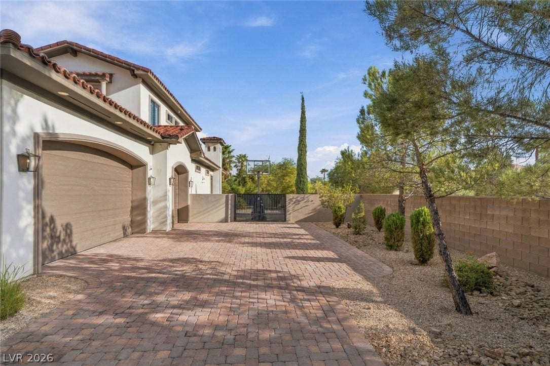 A spacious brick paver driveway leads past the garages toward a gated side yard.