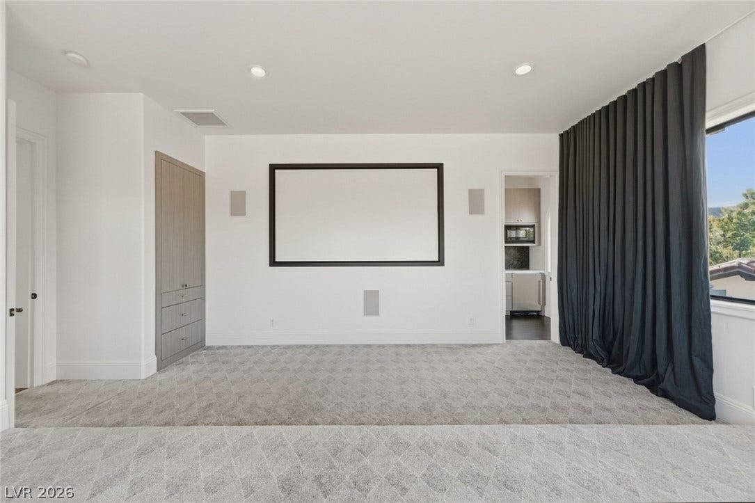 A spacious home theater features recessed lighting, patterned carpeting, and integrated storage solutions.
