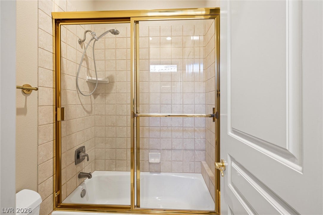 1517 Marbella Ridge Court, Las Vegas, NV 89117 A classic tiled tub shower is enclosed by sliding glass doors with gold-toned framing.