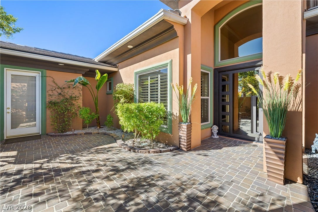 1517 Marbella Ridge Court, Las Vegas, NV 89117 An inviting courtyard entrance welcomes visitors with patterned pavers and stucco exterior walls under blue skies.