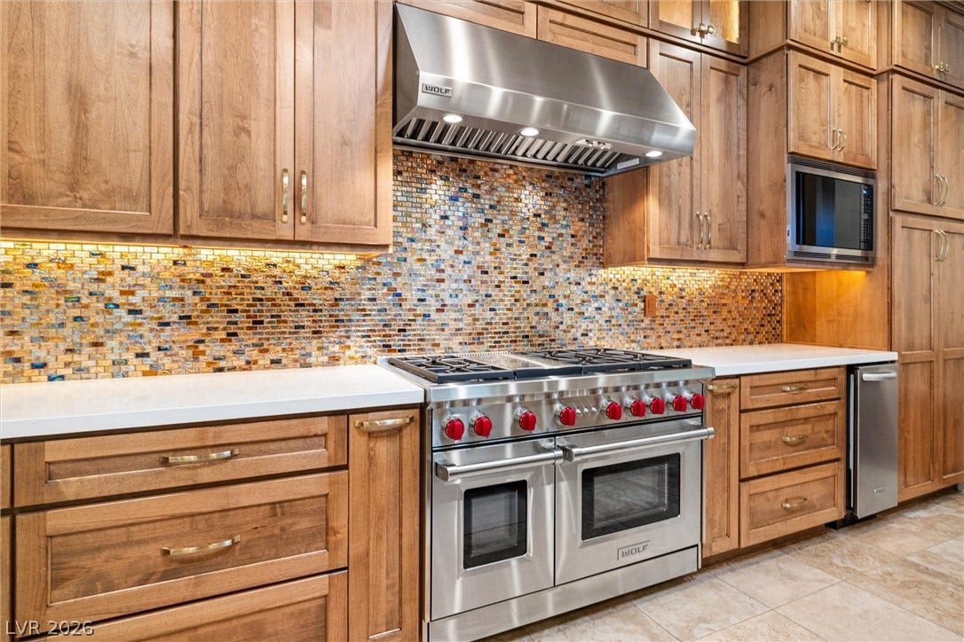 1517 Marbella Ridge Court, Las Vegas, NV 89117 Rich wood cabinetry surrounds a premium gas range beneath a mosaic tile backsplash.