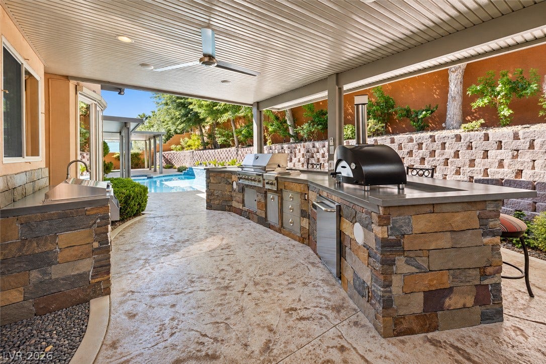1517 Marbella Ridge Court, Las Vegas, NV 89117 A stone-clad outdoor kitchen sits under a covered patio next to a swimming pool.