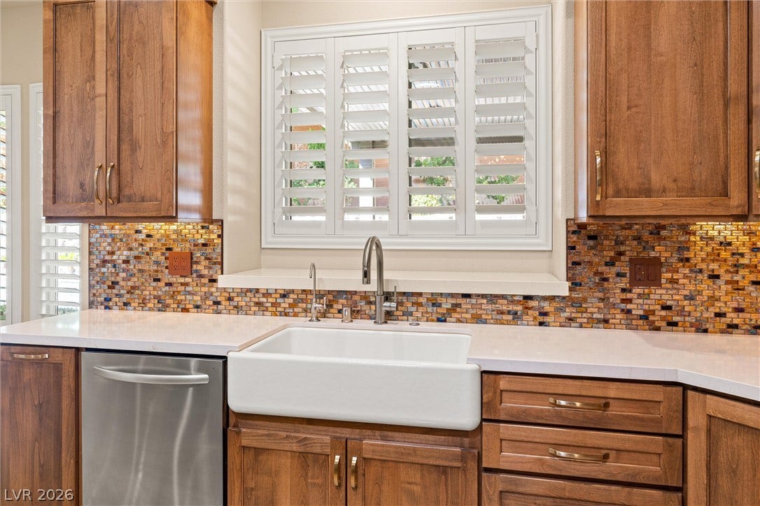 1517 Marbella Ridge Court, Las Vegas, NV 89117 Rich wood cabinetry surrounds a classic farmhouse sink highlighted by a shimmering mosaic tile backsplash.