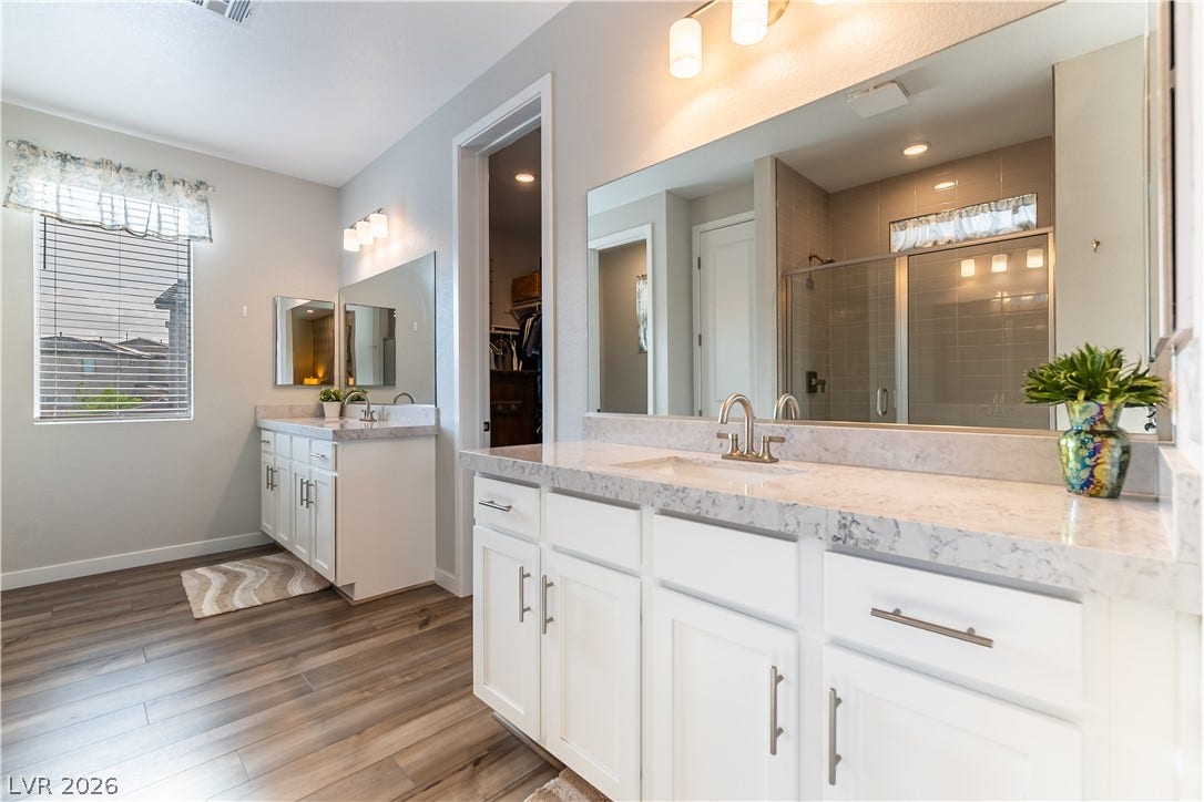 10583 Valletta Avenue, Las Vegas, NV 89166 Double vanities with stone counters and wood-look flooring enhance this primary bath design.