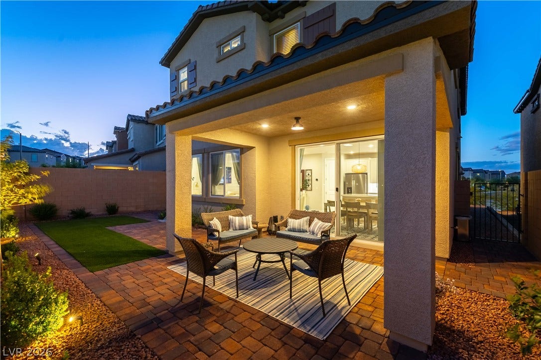 10583 Valletta Avenue, Las Vegas, NV 89166 A covered patio with brick pavers overlooks the landscaped backyard under a twilight sky.