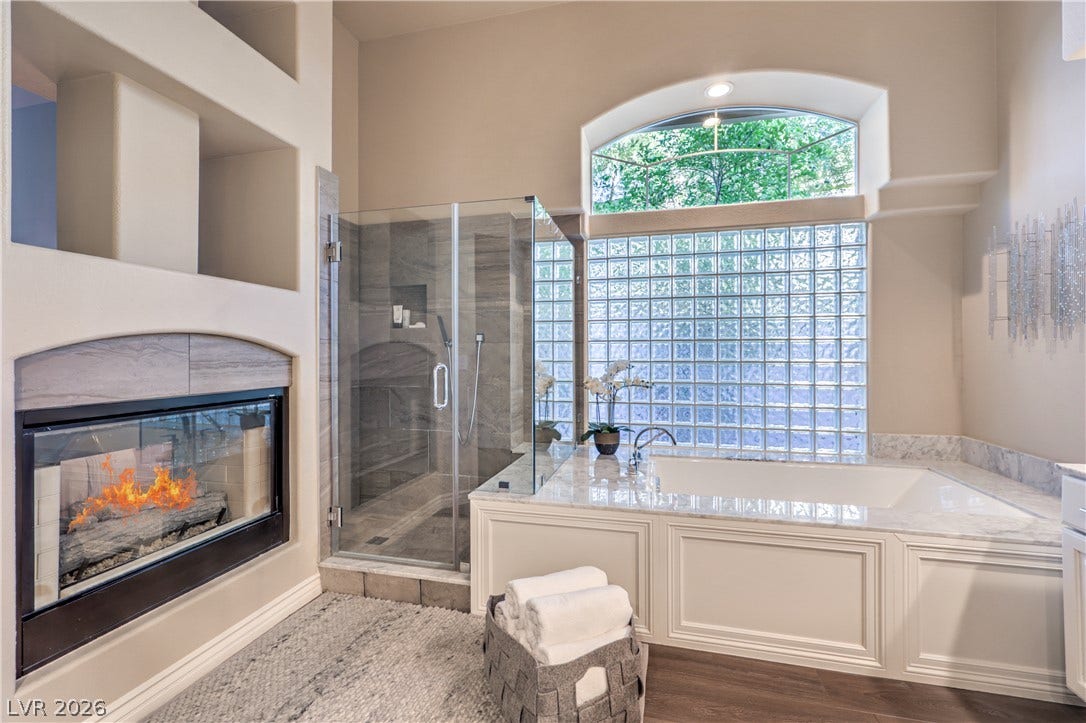 A double-sided fireplace warms this primary bath featuring a soaking tub under glass block windows.