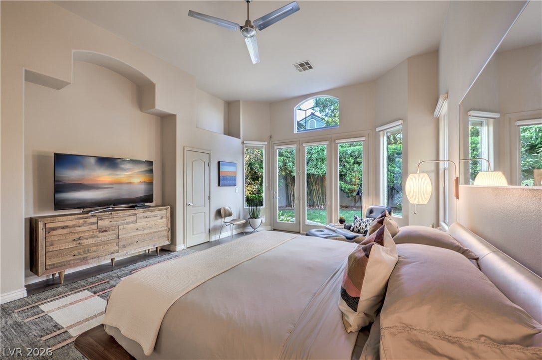 High ceilings and tall windows frame serene backyard views from this bedroom.