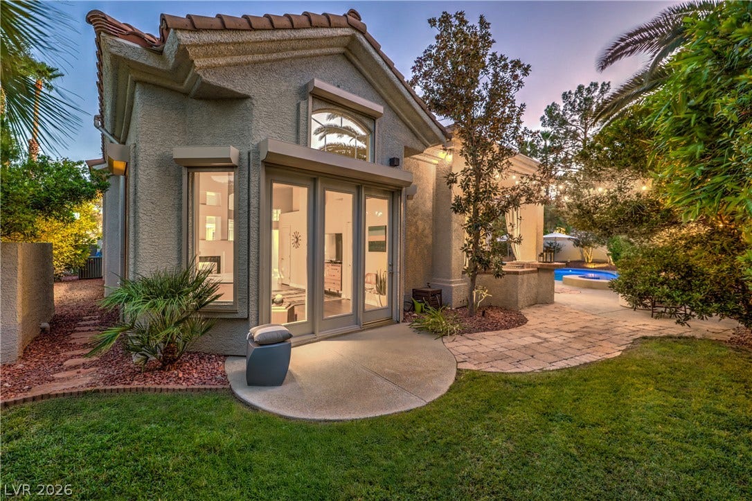 Lush landscaping frames a tiled roof patio overlooking the backyard lawn.