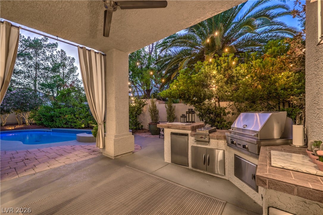 An outdoor kitchen features premium built-in appliances overlooking a glistening pool area.