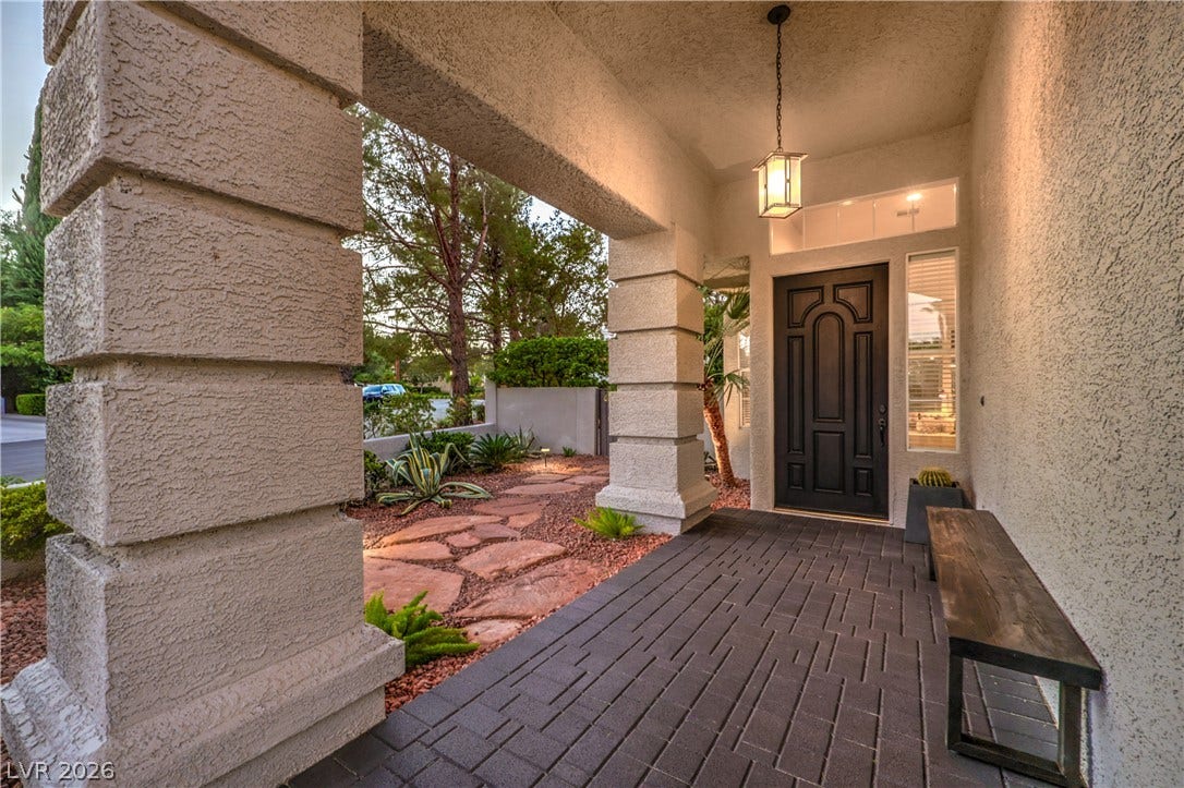 A covered entry porch with textured stucco pillars and paved flooring leads to the front door.