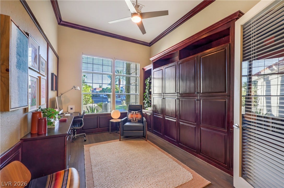 Rich wood built-ins and matching trim frame this versatile workspace beneath a tray ceiling.