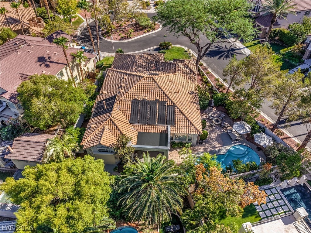 Lush landscaping surrounds this classic tile roof home featuring a backyard pool and patio area.