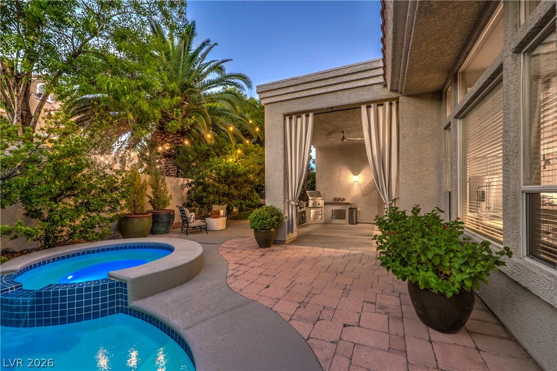 A private backyard oasis features custom stone paving, a spa, and a built-in outdoor kitchen.