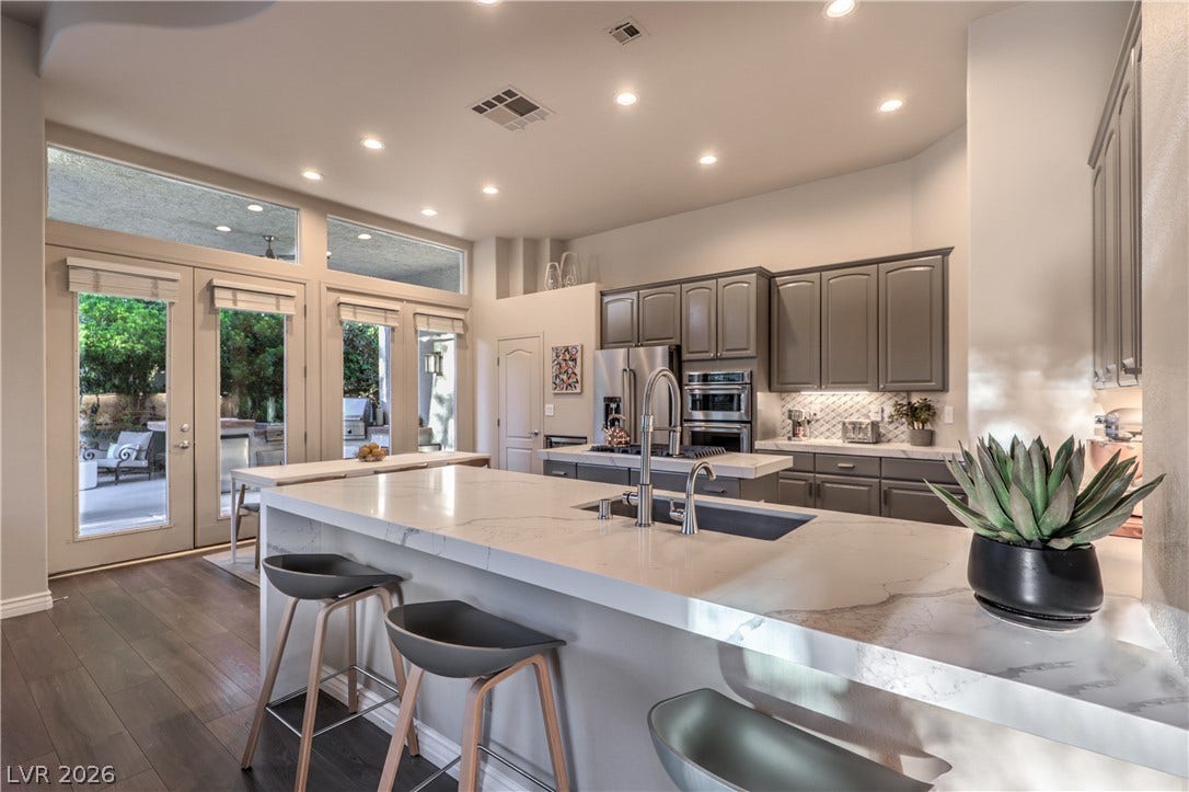 An expansive kitchen features high ceilings, stone counters, and elegant wood flooring.