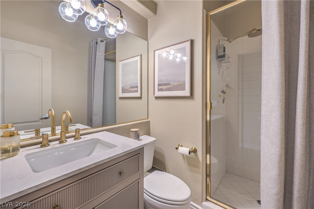A glass-enclosed walk-in shower complements the single vanity with golden brass fixtures.