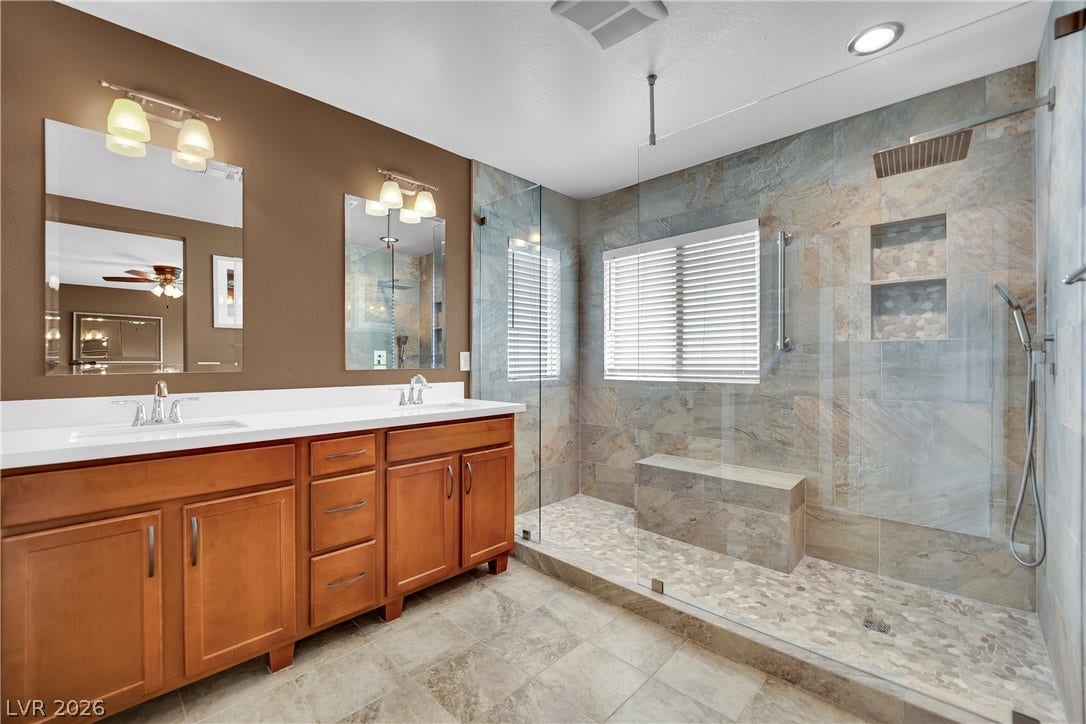 1421 Lamance Court, North Las Vegas, NV 89031 A spacious stone tile shower with built-in bench seating anchors this dual vanity bathroom.
