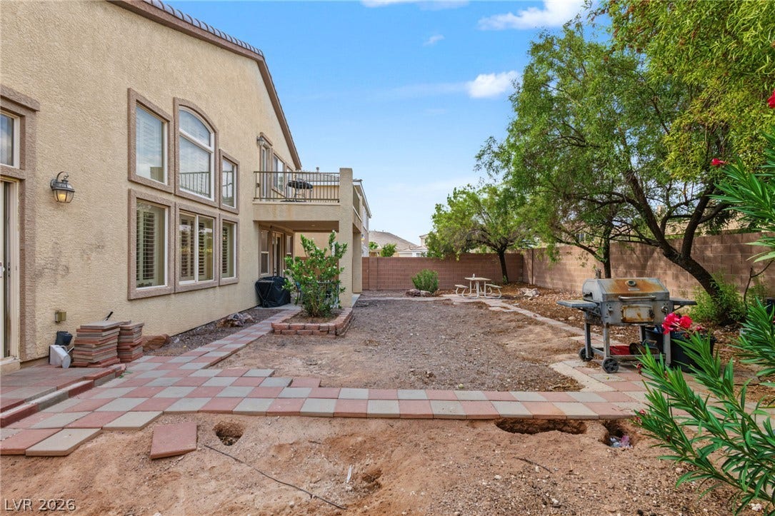 7021 Albatross Attic Street, North Las Vegas, NV 89084 A spacious backyard area features a paved walkway, mature trees, and a second-level balcony.