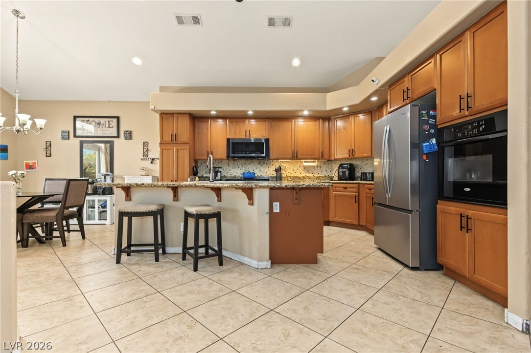 7021 Albatross Attic Street, North Las Vegas, NV 89084 Warm wood cabinetry and neutral tile flooring anchor this functional kitchen layout.
