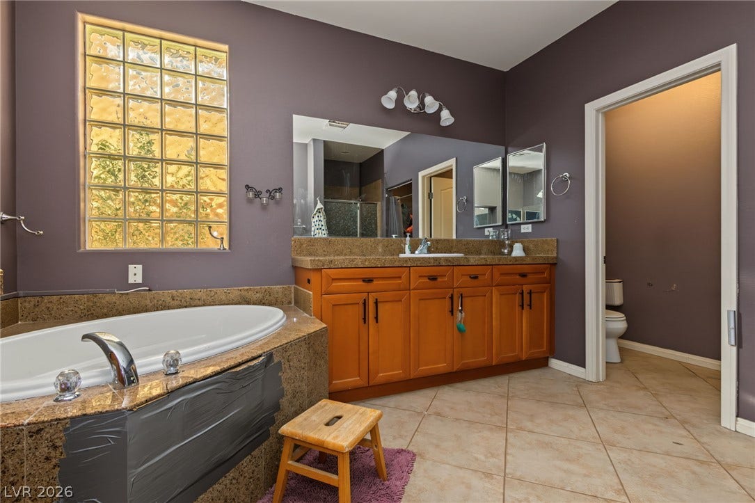 7021 Albatross Attic Street, North Las Vegas, NV 89084 A deep soaking tub sits beneath a textured glass block window in this spacious bathroom.