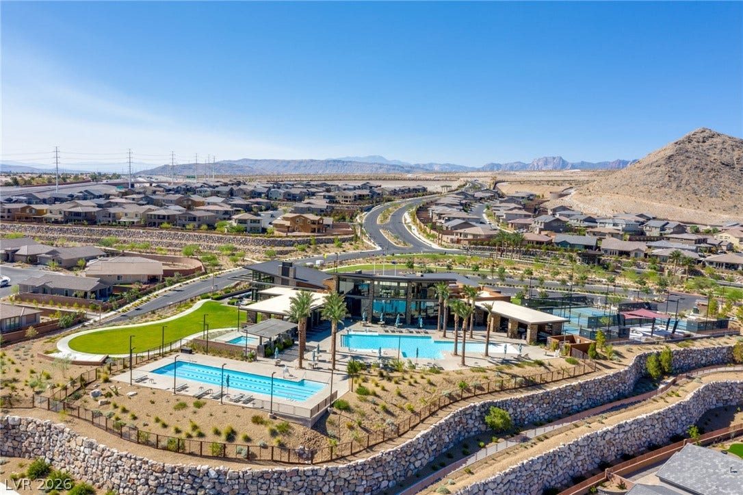 An aerial perspective reveals a vibrant community hub with multiple pools and tennis courts, set against a backdrop of desert mountains and residential homes.