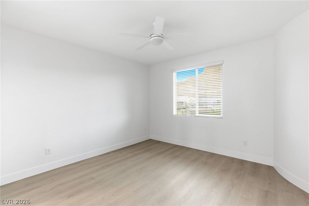 A well-lit bedroom features durable laminate flooring and a ceiling fan for comfort.