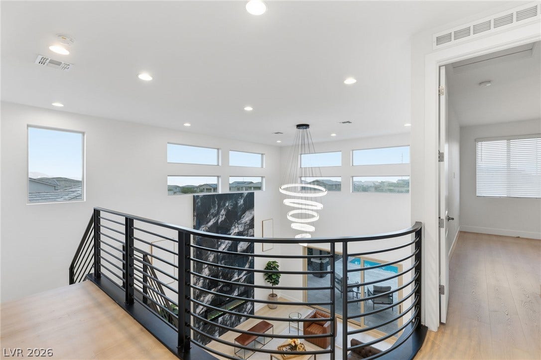 A grand stairway with a sleek metal railing overlooks a spacious living area, bathed in light from strategically placed windows.