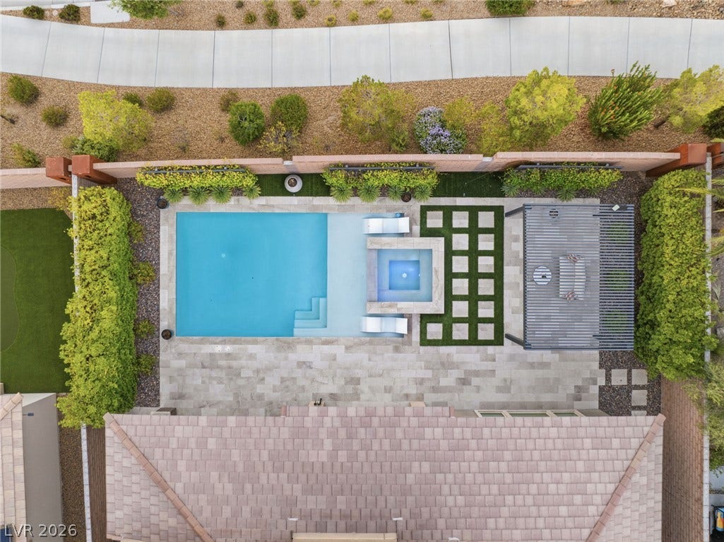 An aerial perspective reveals a serene backyard oasis featuring a pool, spa, and pergola-covered lounge area.