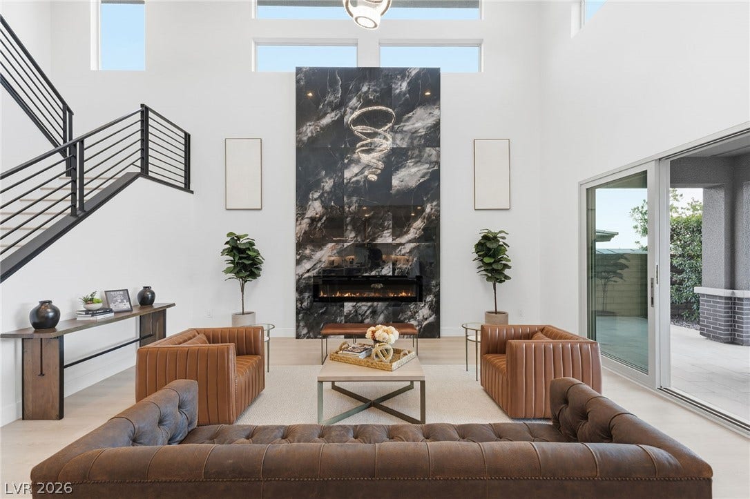 A dramatic marble-clad fireplace anchors this airy living space with soaring ceilings and an elegant modern staircase.