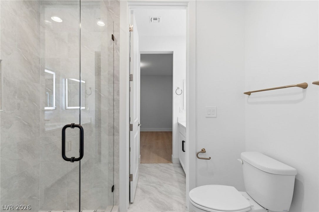 A sleek, contemporary bathroom features a glass-enclosed shower and modern fixtures, leading to a bright hallway.
