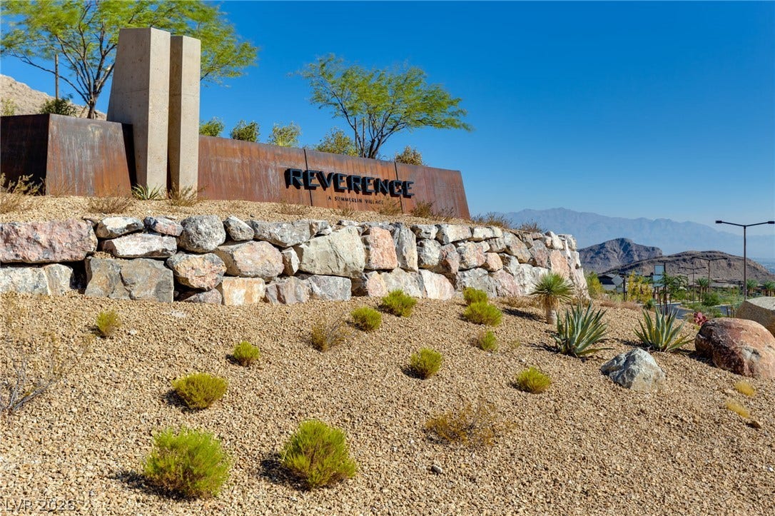 A striking rock wall with desert landscaping creates a grand entrance to this community, framed by distant mountains.