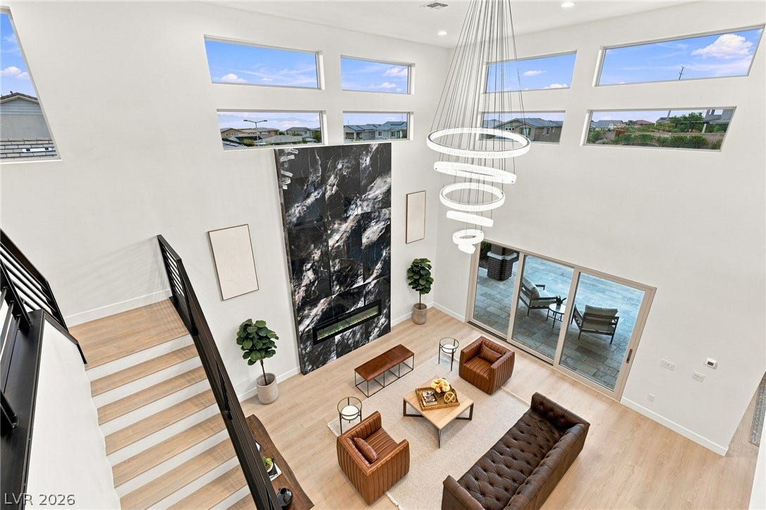 An airy living room boasts a dramatic marble-clad fireplace, high ceilings, and expansive windows.